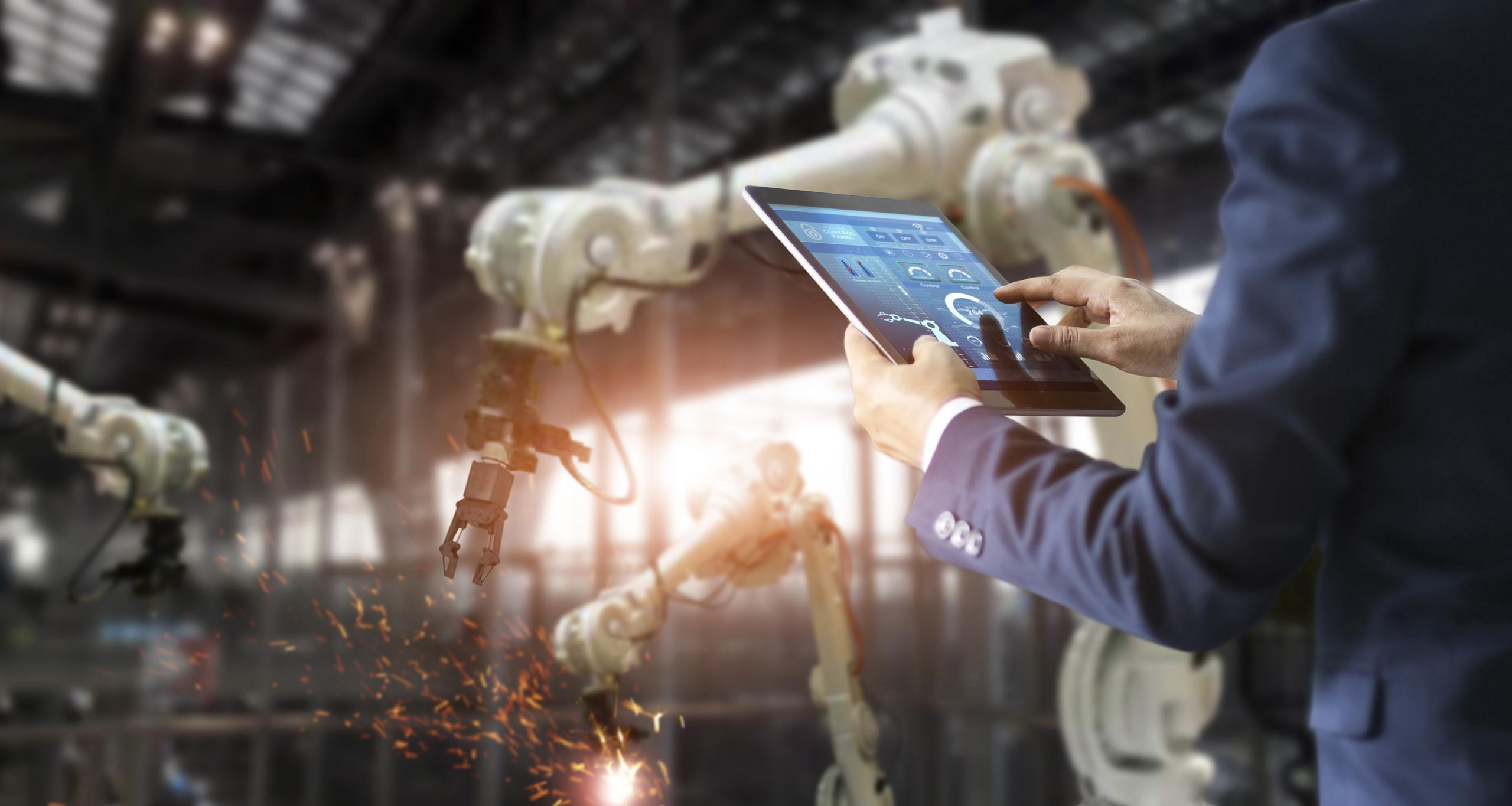 Manager industrial engineer using tablet check and control automation robot arms machine in intelligent factory industrial on real time monitoring system software. Welding robotics and digital manufacturing operation. Industry 4.0 concept